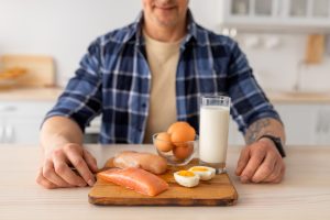 Homem diante de uma tábua com alimentos ricos em proteína para um cardápio saudável.
