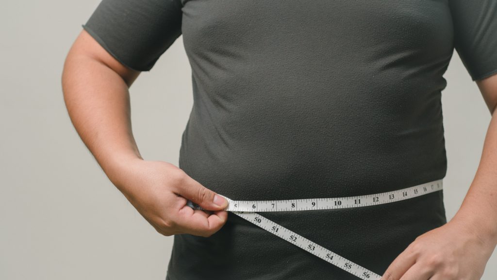 Homem com excesso de peso medindo a circunferência abdominal com fita métrica, um indicador de gordura visceral.
