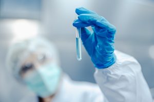 Profissional com luvas azuis segurando tubo de ensaio com líquido em laboratório