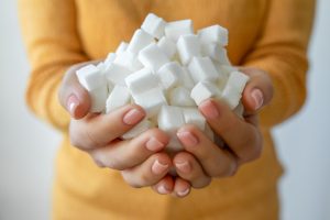 Close em mãos segurando uma grande quantidade de cubos de açúcar branco, ilustrando o alto consumo de açúcar que atua como um fator de risco para o pré-diabetes.