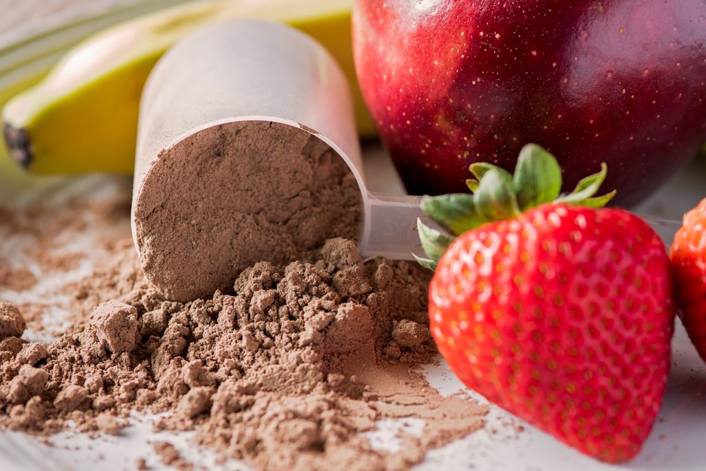 Frutas frescas ao lado de scoop com whey protein em pó sobre bancada.